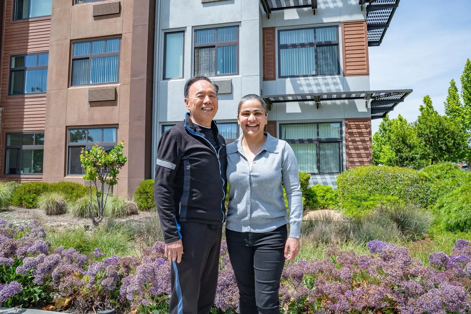 Two people standing in a garden courtyard outside an apartment building
