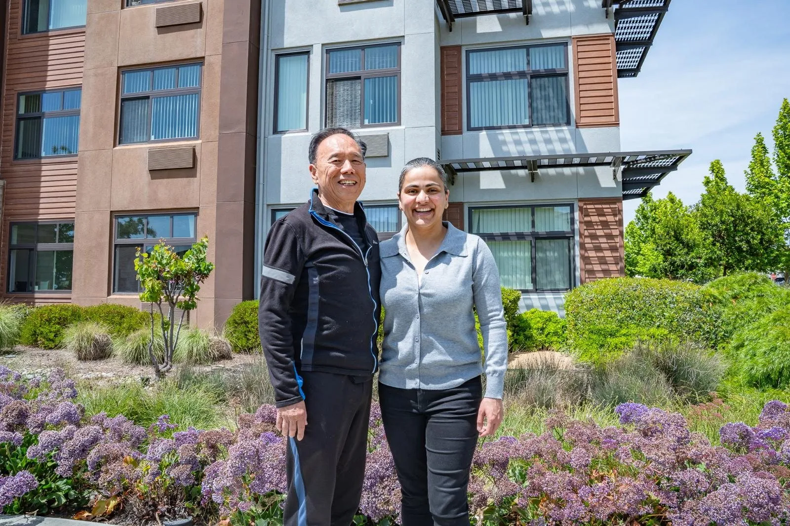 Two people standing in a garden courtyard outside an apartment building