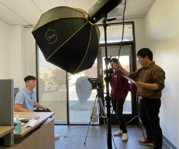 A Foundation team member being filmed under a studio softbox while two crew members set up the shot